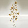 Gold-finished metal wall sculpture depicting an abstract, branching vine structure with multiple circular, stylized sand dollar shapes of varying sizes. The piece is mounted vertically against a pale background.