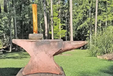 A rustic metal anvil with a hammer balanced on top.