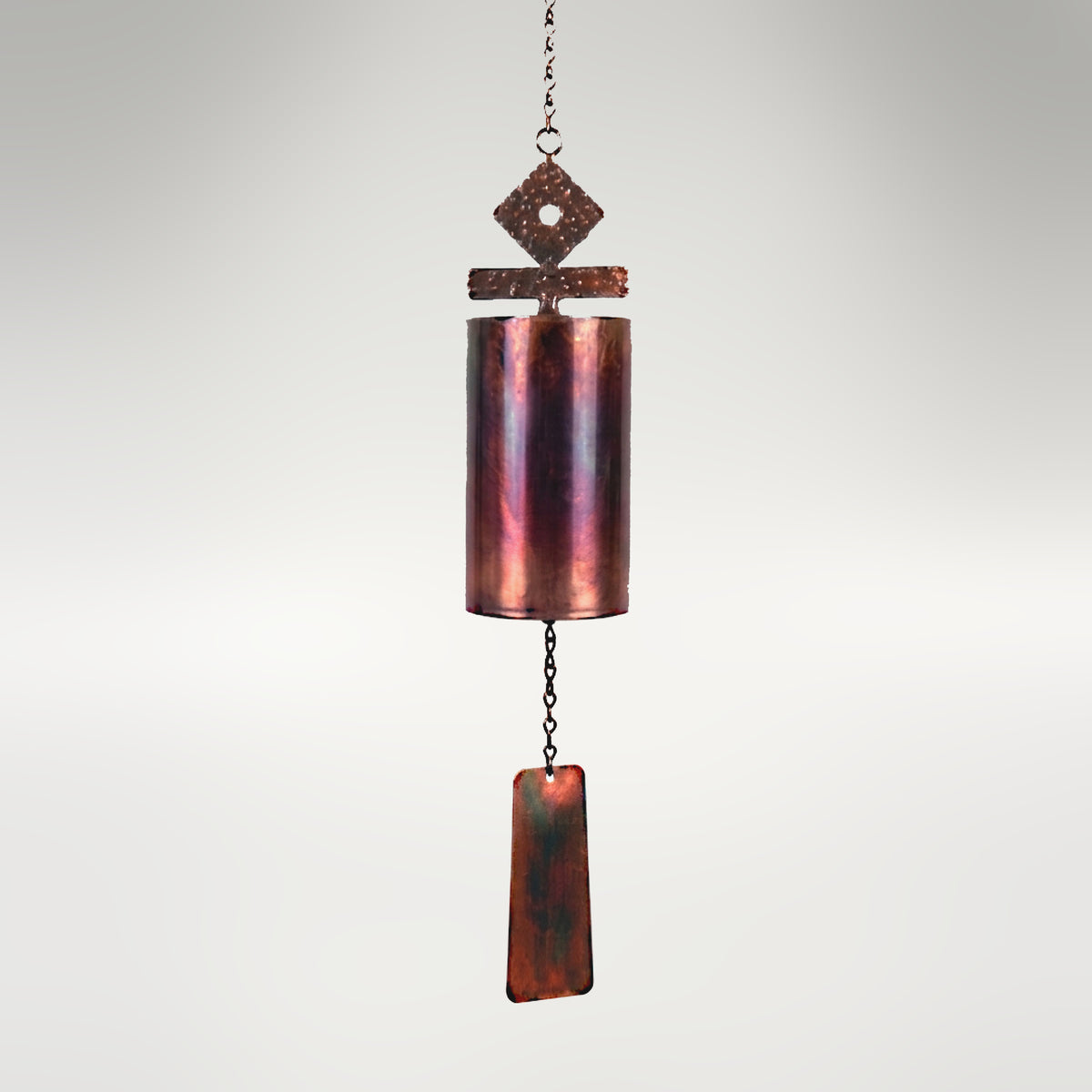 Cylindrical copper wind bell with an iridescent patina, featuring a geometric top ornament and a dangling rectangular wind catcher..